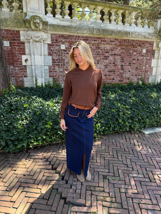 Another view of blue denim maxi skirt with chestnut leather trim detail, front flap pockets and zipper closure slit