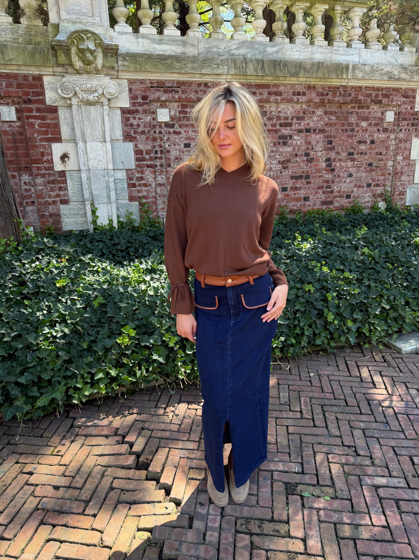 Front view of blue denim maxi skirt with chestnut leather trim detail, front flap pockets and zipper closure slit