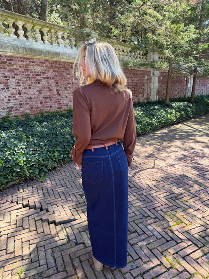 Back view of blue denim maxi skirt with chestnut leather trim detail, front flap pockets and zipper closure slit