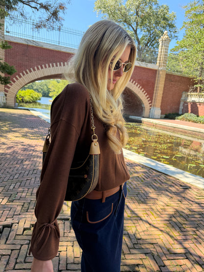Side view of chestnut v-neck sweater with tie sleeve detail tucked into skirt