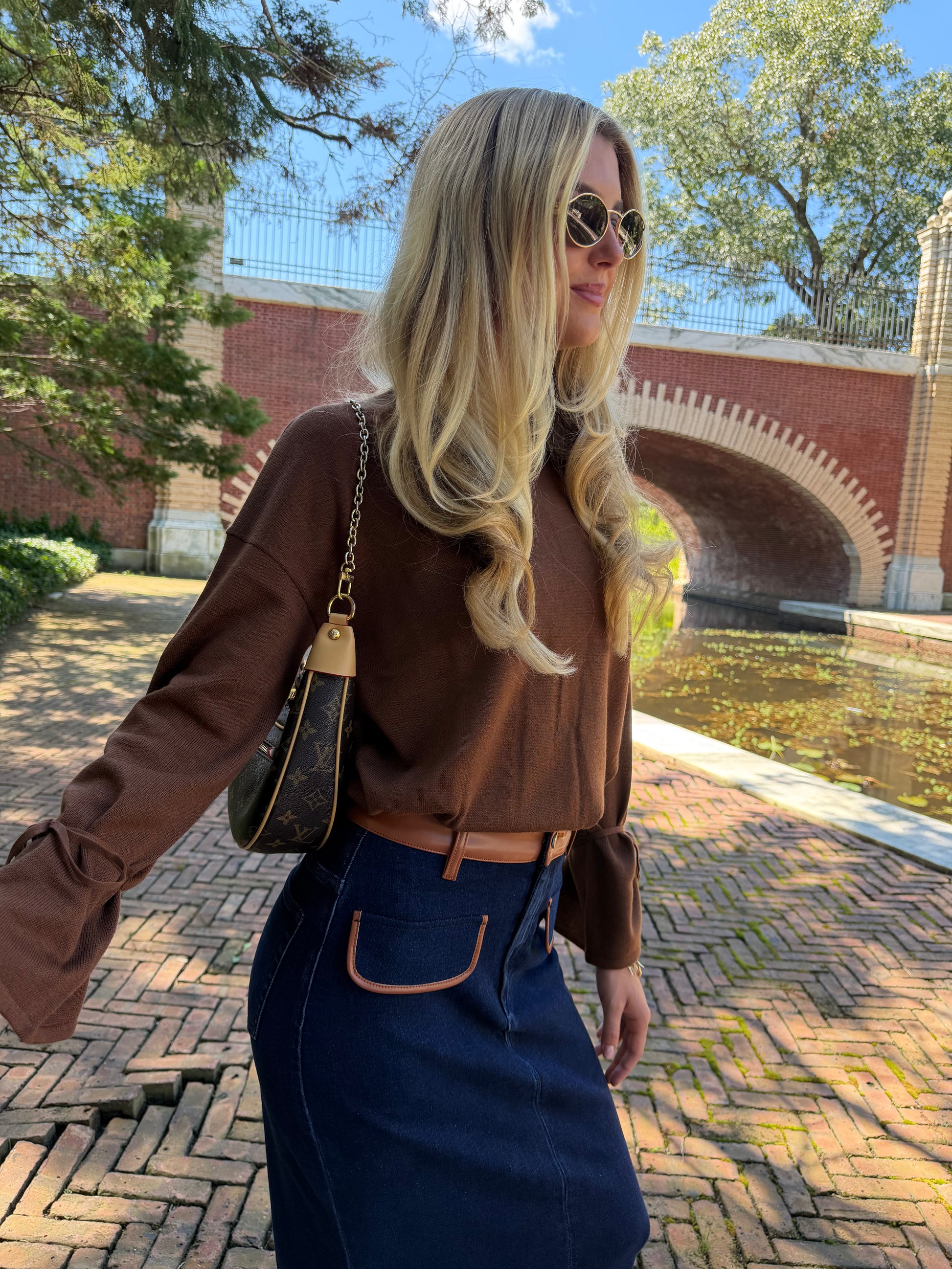 Second side view of chestnut v-neck sweater with tie sleeve detail tucked into skirt