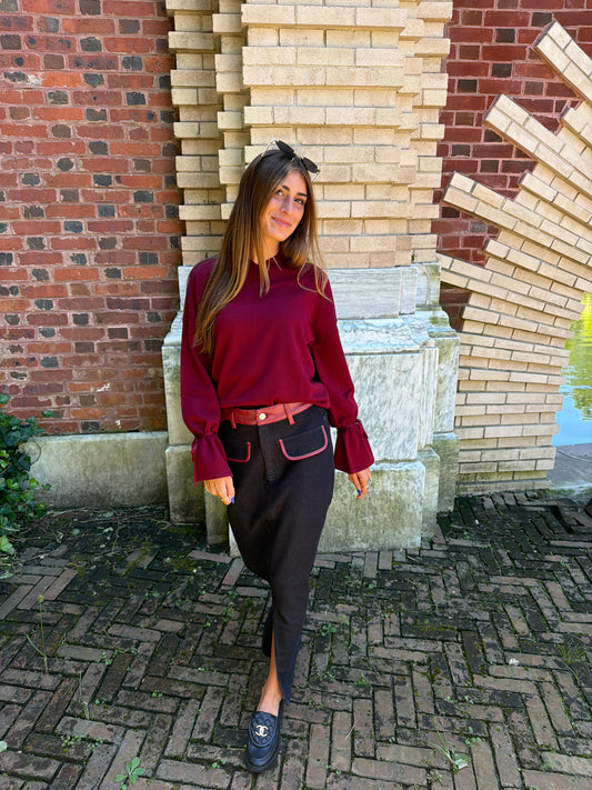 In motion view of black denim maxi skirt with burgundy leather trim detail, front flap pockets and zipper closure slit